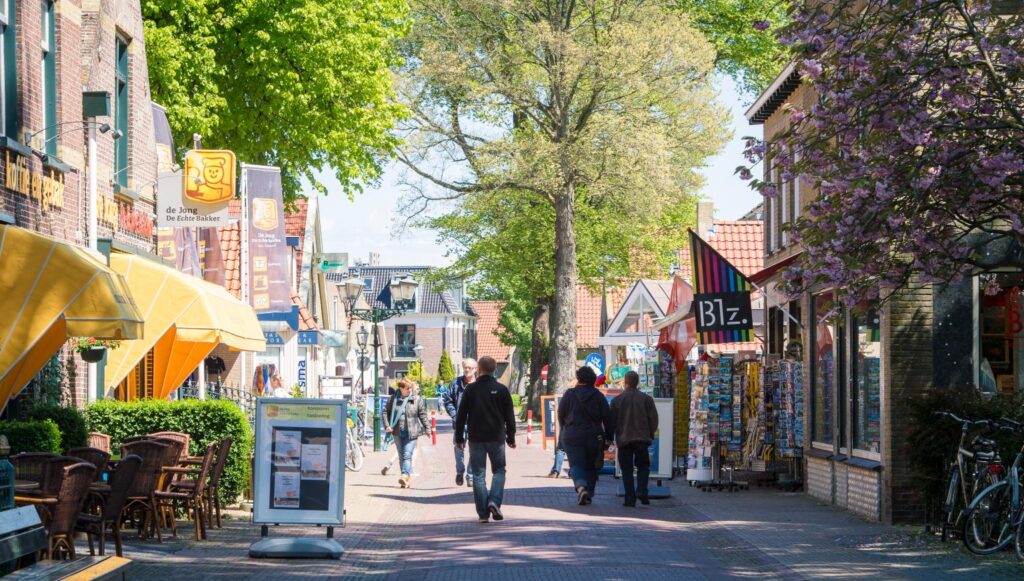 Toeristen wandelen en fietsen door gezellige winkelstraat met terrassen en winkels