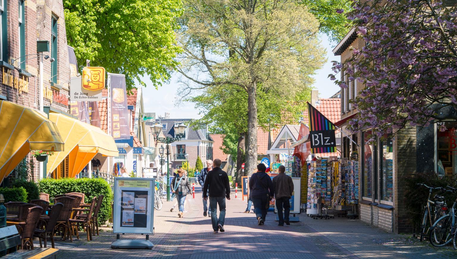 Toeristen wandelen en fietsen door gezellige winkelstraat met terrassen en winkels