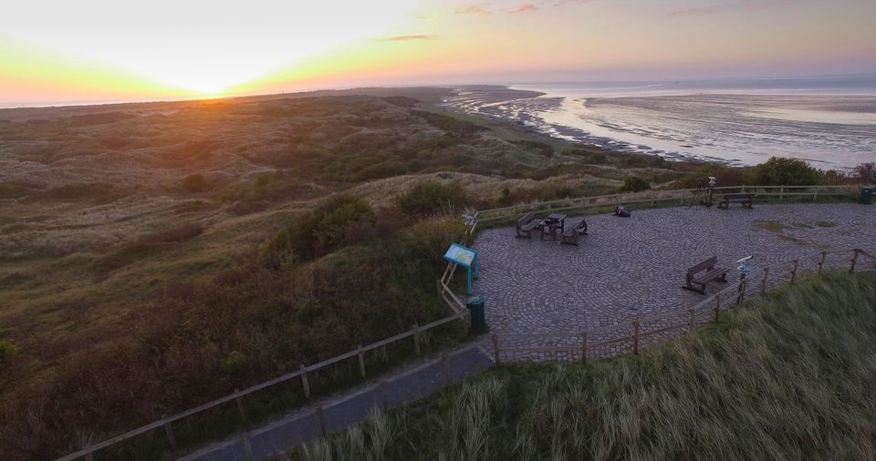 Fietsers genieten van zonsondergang op Ameland uitkijkpunt met zeezicht en duinlandschap